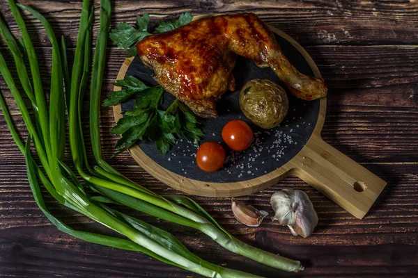 Izgara tavuk, patates, domates, salata, yeşil soğan ve taş plaka üzerinde tuz. Ahşap arka planda ızgara gıda. 