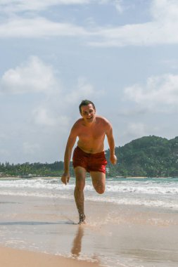 2011.05.06, Phuket, Tayland. Avrupalı turist kırmızı yüzme iç çamaşırı giyen çalışan ve plajda atlama. Asya'da seyahat.