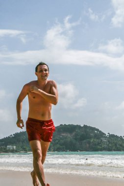 2011.05.06, Phuket, Tayland. Avrupalı turist kırmızı yüzme iç çamaşırı giyen çalışan ve plajda atlama. Asya'da seyahat.
