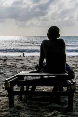 2011.05.06, Phuket, Tayland. Sahilde şezlongda oturan küçük çocuğun silueti, arka yan görünüm ve tahıl etkisi. 