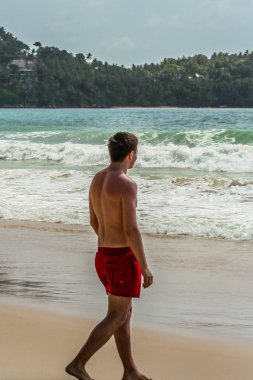 2011.05.06, Phuket, Tayland. Avrupalı turist kırmızı yüzme iç çamaşırı giyiyor ve sahil şeridinde yürüyor. Asya'da seyahat.