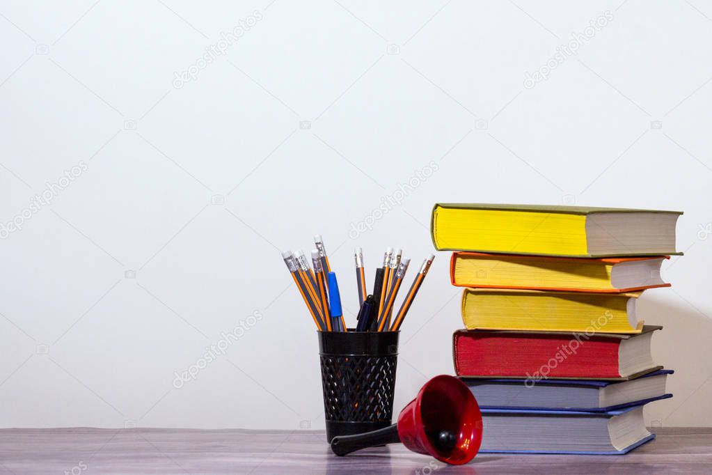 Concept of education and preparation for school. Stack of colorful books, red school bell and pencils on background of white. Beginning of school year.