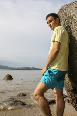 2011.05.07, Phuket, Tayland. Asya'yı dolaşın. Phuket sahilinde taşın yanında duran bir Rus adam, yan görüş.