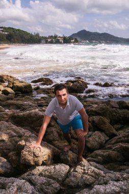 2011.05.08, Phuket, Tayland. Okyanus dalgalarının arka planında kayaların üzerinde duran genç bir adam. Asya'nın aktif turizmi.