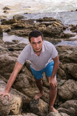 2011.05.08, Phuket, Tayland. Okyanus dalgalarının arka planında kayaların üzerinde duran genç bir adam. Asya'nın aktif turizmi.