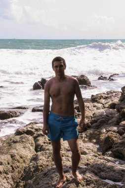 2011.05.08, Phuket, Tayland. Okyanus dalgalarının arka planında kayaların üzerinde duran genç bir adam. Asya'nın aktif turizmi.