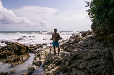 2011.05.08, Phuket, Tayland. Okyanus dalgalarının arka planında kayaların üzerinde duran genç bir adam. Asya'nın aktif turizmi.
