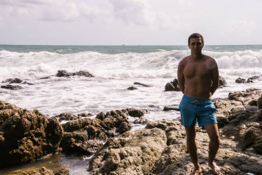 2011.05.08, Phuket, Tayland. Okyanus dalgalarının arka planında kayaların üzerinde duran genç bir adam. Asya'nın aktif turizmi.