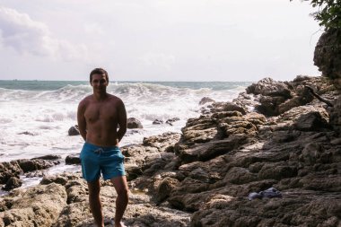 2011.05.08, Phuket, Tayland. Okyanus dalgalarının arka planında kayaların üzerinde duran genç bir adam. Asya'nın aktif turizmi.