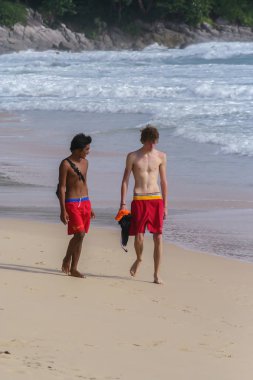 2011.05.08, Phuket, Tayland. Okyanus kıyısında yürüyen iki genç adam. Asya Turizmi. Avustralyalı ve Asyalı gençler sahilde.