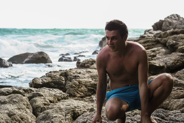 2011.05.08, Phuket, Tayland. Okyanus dalgalarının arka planında kayaların üzerinde oturan genç bir adam. Asya Turizm.