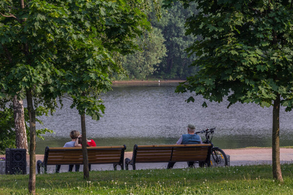 2019.05.31, Moscow, Russia. Group of people sitting on the bench at river bank. Walking after work