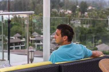 2011.05.10, Phuket, Tayland. Otelin çatısındaki kanepede oturan genç bir adam. Kameraya bakan bir adam. Phuket Turizm.