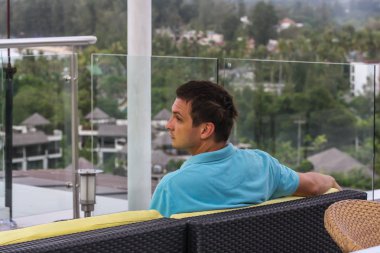 2011.05.10, Phuket, Tayland. Otelin çatısındaki kanepede oturan genç bir adam. Kameraya bakan bir adam. Phuket Turizm.