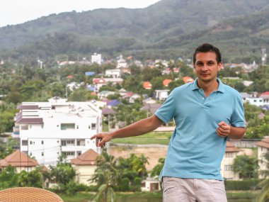 2011.05.10, Phuket, Tayland. Otelin çatısında cam çitlerin yanında duran genç bir adam. Phuket plajının arka planında kameraya bakan bir adam.