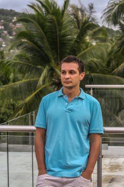 2011.05.10, Phuket, Tayland. Otelin çatısında cam çitlerin yanında duran genç bir adam. Phuket plajının arka planında kameraya bakan bir adam.