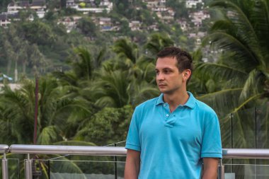 2011.05.10, Phuket, Tayland. Otelin çatısında cam çitlerin yanında duran genç bir adam. Phuket plajının arka planında kameraya bakan bir adam.