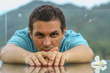 2011.05.10, Phuket, Tayland. Phuket doğanın backgrounf üzerinde cam masa nın yanında oturan genç bir adamın portresi.