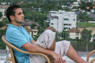 2011.05.10, Phuket, Tayland. Köyün arka planında otelin çatısındaki koltukta oturan genç bir adam. Phuket Turizm.