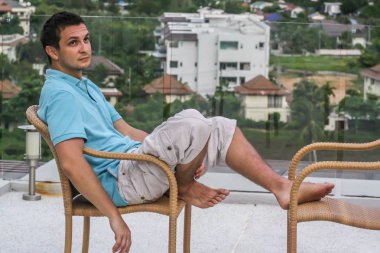 2011.05.10, Phuket, Tayland. Köyün arka planında otelin çatısındaki koltukta oturan genç bir adam. Phuket Turizm.