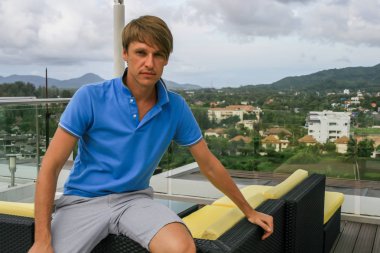 2011.05.10, Phuket, Tayland. Otelin çatısındaki kanepede oturan genç bir adam. Kameraya bakan bir adam. Phuket Turizm.