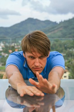 2011.05.10, Phuket, Tayland. Phuket doğanın backgrounf ellerini arkasında saklanan cam masanın yanında oturan genç bir adamın portresi.