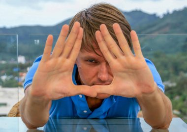 2011.05.10, Phuket, Tayland. Phuket doğanın backgrounf ellerini arkasında saklanan cam masanın yanında oturan genç bir adamın portresi.