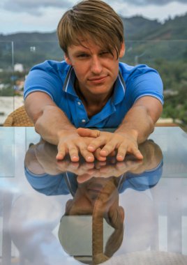 2011.05.10, Phuket, Tayland. Bir masada oturan ve önünde ellerini uzatan genç bir adamın portresi. Asya'da seyahat.