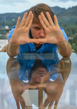 2011.05.10, Phuket, Tayland. Phuket doğanın backgrounf ellerini arkasında saklanan cam masanın yanında oturan genç bir adamın portresi.