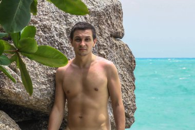 2011.05.10, Phuket, Tayland. Okyanus kıyısındakayanın arka planında duran üstsüz genç bir adam..