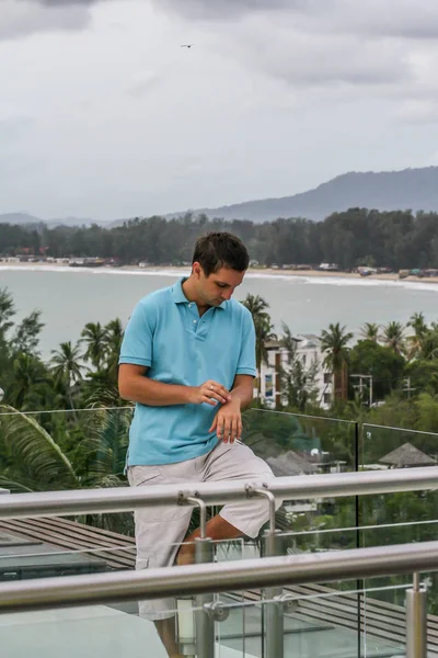 2011.05.10, Phuket, Tayland. Otelin çatısında cam çitlerin yanında duran genç bir adam. Phuket plajının arka planında kameraya bakan bir adam.