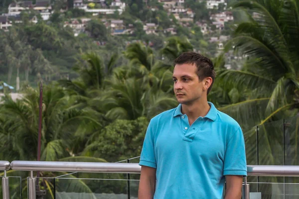 2011.05.10, Phuket, Tayland. Otelin çatısında cam çitlerin yanında duran genç bir adam. Phuket plajının arka planında kameraya bakan bir adam.