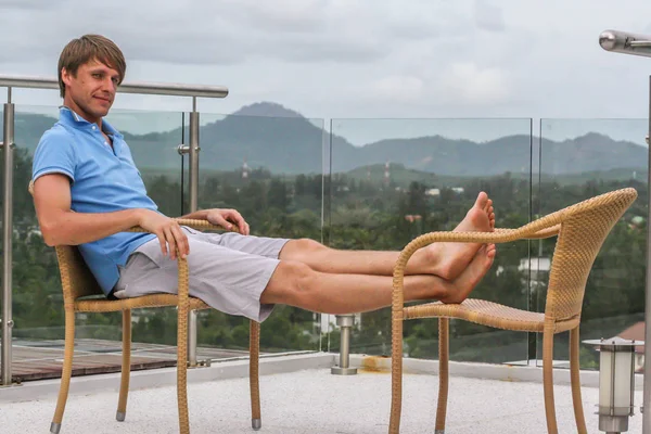 2011.05.10, Phuket, Tayland. Köyün arka planında otelin çatısındaki koltukta oturan genç bir adam. Phuket Turizm.