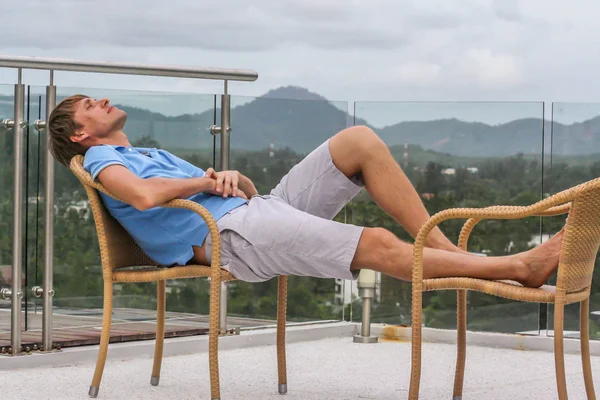 2011.05.10, Phuket, Tayland. Köyün arka planında otelin çatısındaki koltukta oturan genç bir adam. Phuket Turizm. Gökyüzüne bakan bir adam..