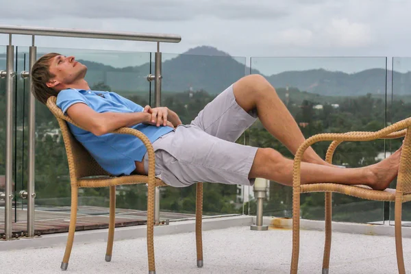 2011.05.10, Phuket, Tayland. Köyün arka planında otelin çatısındaki koltukta oturan genç bir adam. Phuket Turizm. Gökyüzüne bakan bir adam..
