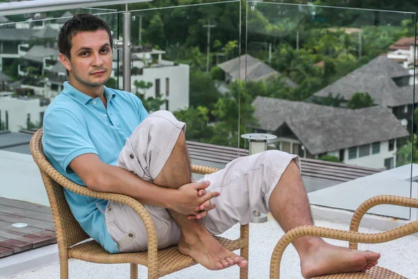 2011.05.10, Phuket, Tayland. Köyün arka planında otelin çatısındaki koltukta oturan genç bir adam. Phuket Turizm.