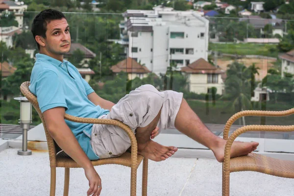 2011.05.10, Phuket, Tayland. Köyün arka planında otelin çatısındaki koltukta oturan genç bir adam. Phuket Turizm.