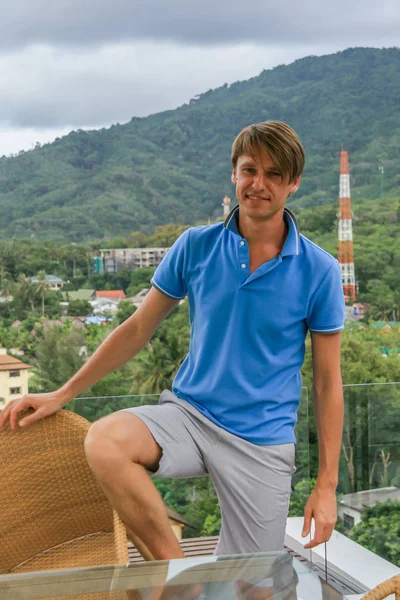 2011.05.10, Phuket, Tayland. Otelin çatısında cam çitlerin yanında duran genç bir adam. Kameraya bakan bir adam. Phuket Turizm.