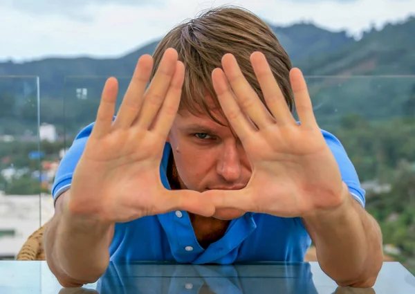 2011.05.10, Phuket, Tayland. Phuket doğanın backgrounf ellerini arkasında saklanan cam masanın yanında oturan genç bir adamın portresi.