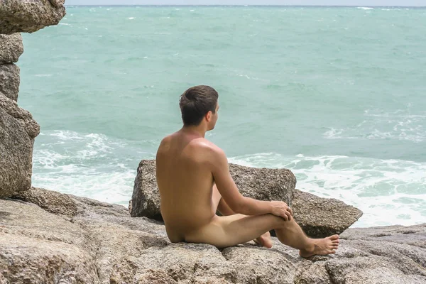 2011.05.10, Phuket, Tayland. Genç, çıplak bir adam kayaların üzerinde oturuyor ve okyanusa bakıyor. Yaz sahilde istirahat. 