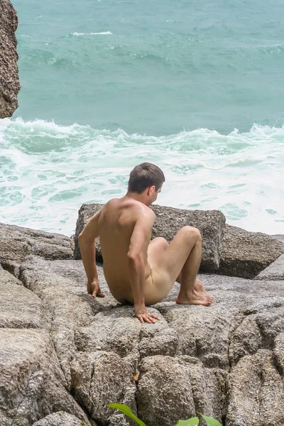 2011.05.10, Phuket, Tayland. Genç, çıplak bir adam kayaların üzerinde oturuyor ve okyanusa bakıyor. Yaz sahilde istirahat. 