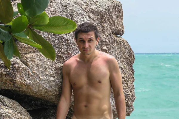 2011.05.10, Phuket, Tayland. Okyanus kıyısındakayanın arka planında duran üstsüz genç bir adam..