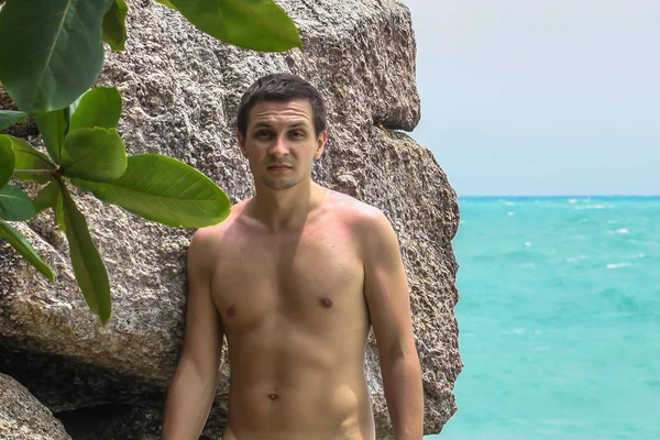2011.05.10, Phuket, Tayland. Okyanus kıyısındakayanın arka planında duran üstsüz genç bir adam..