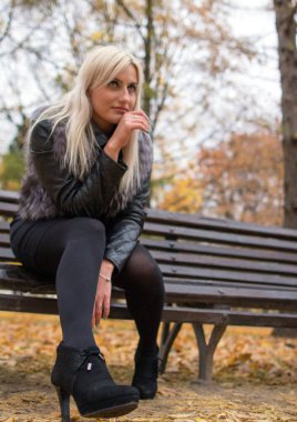 2017.10.21, Moskova, Rusya. Düşen parkta bankta oturan kitap tutan kürk siyah ceket giyen genç bir çekici kadın. Sonbahar parkı etrafında yürüyüş.
