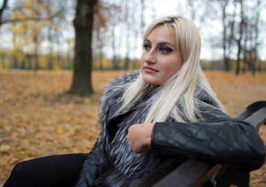 2017.10.21, Moskova, Rusya. Düşen parkta bankta oturan kitap tutan kürk siyah ceket giyen genç bir çekici kadın. Sonbahar parkı etrafında yürüyüş.
