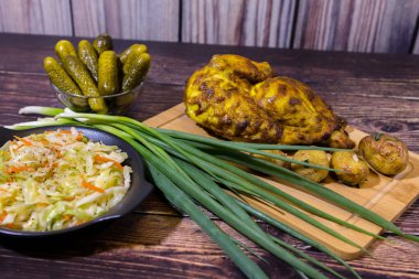 Gıda (turşu, lahana turşusu, kızarmış tavuk, yeşil soğan ve kızarmış patates) ahşap masada. Yemek masası yakın.