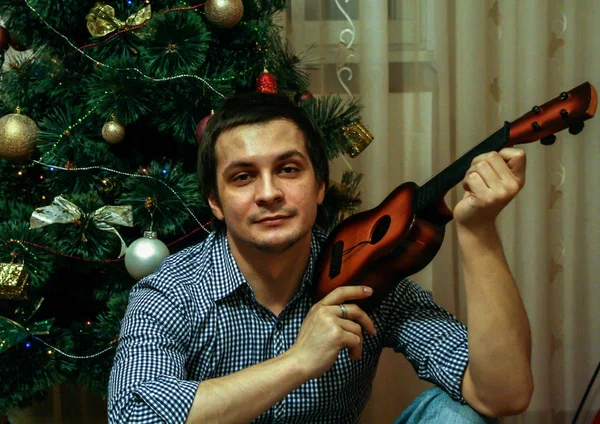 2011 01ロシアのMaloyaroslavets 若い男はおもちゃのギターを持っています新年の木 ぼかし 穀物効果の背景に座って — ストック写真