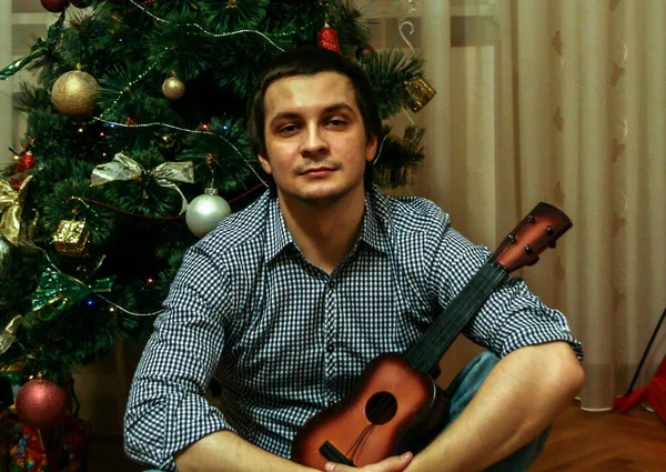 2011,01.01, Maloyaroslavets, Rusya. Genç bir adam yeni yıl ağacının arka planında oyuncak gitar tutuyor. Bulanık ve tahıl etkisi..