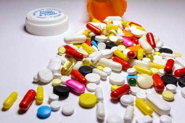 Farklı şekillerde, boyutlarda ve renklerde haplar, açık arkaplanda turuncu bir şişeden yayılmış..