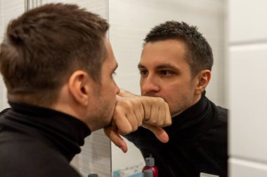 Siyah balıkçı yaka giyen ve aynaya bakan kısa saçlı genç bir adamın portresi. Aynaya bakan genç bir adamın yansıması..